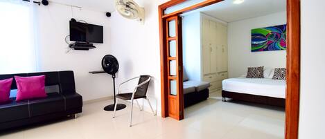 A modern living room with a black sofa, a chair, a TV, and a fan.