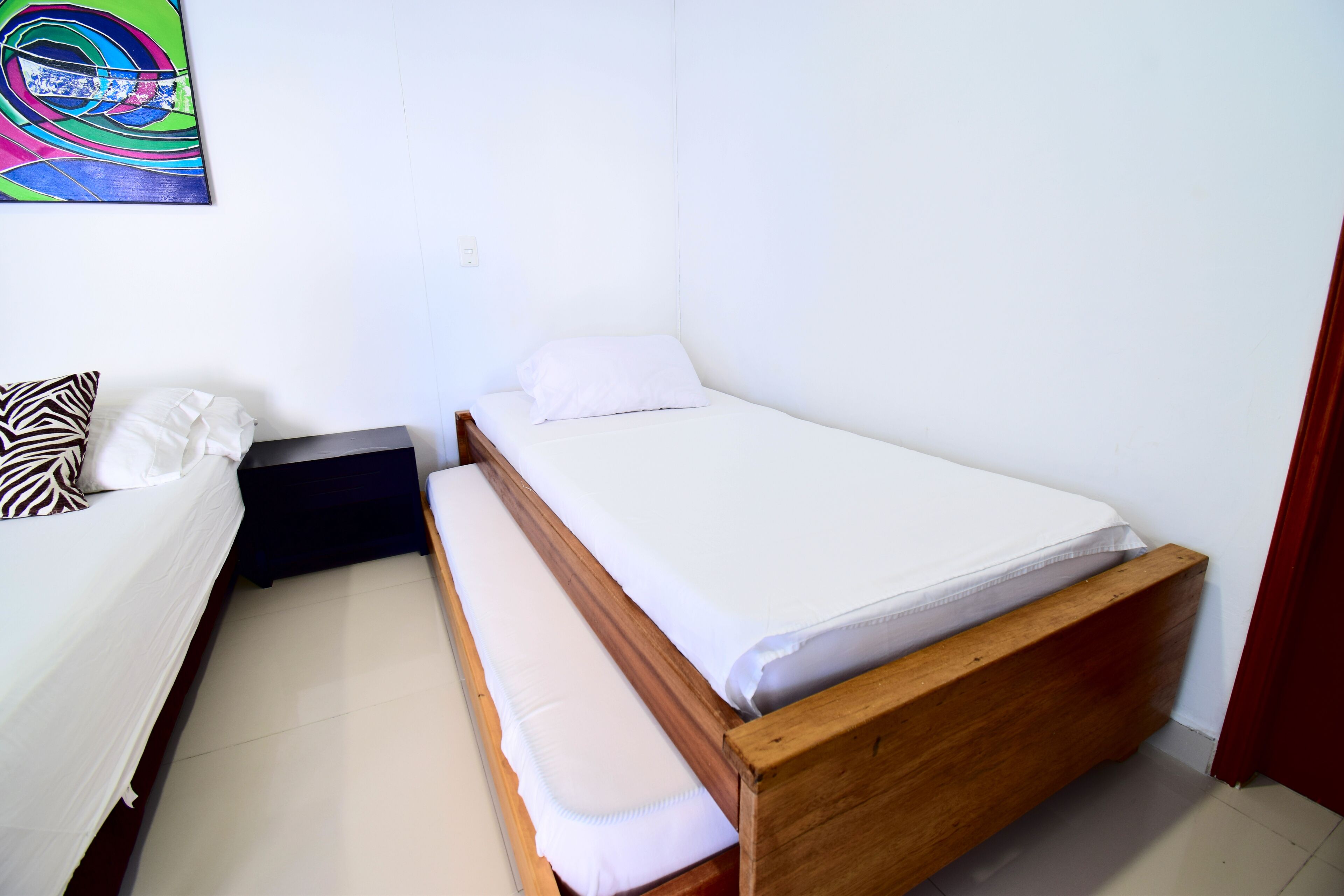 Une petite chambre avec un lit simple, un cadre en bois, du linge de lit blanc et un coussin à motifs zébrés.