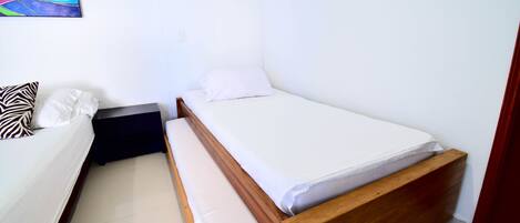 Une petite chambre avec un lit simple, un cadre en bois, du linge de lit blanc et un coussin à motifs zébrés.