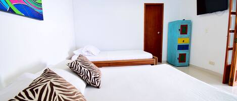Habitación de hotel con dos camas, un cuadro abstracto colorido, un televisor y un mueble azul con cajones.