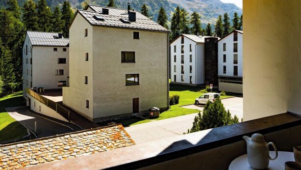 A view of a modern building complex with multiple white structures, a paved driveway, and a mountainous backdrop. - Chesa Maurus A5 by Interhome (St. Moritz)