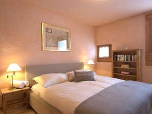 A bedroom with a bed, two bedside lamps, a map on the wall, a bookshelf, and a window. - Chesa Maurus A5 by Interhome (St. Moritz)