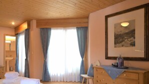 A hotel room with a wooden ceiling, a bed with white linens, a wooden dresser, a chair, and a framed picture on the wall. - Chesa Maurus A5 by Interhome (St. Moritz)