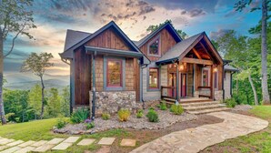 A two-story house with a stone foundation, wooden siding, and a stone pathway leading to the entrance. - Luxury 3BR Mountain Cabin • Hot Tub • Game Room • Outdoor Fireplace (Epworth)