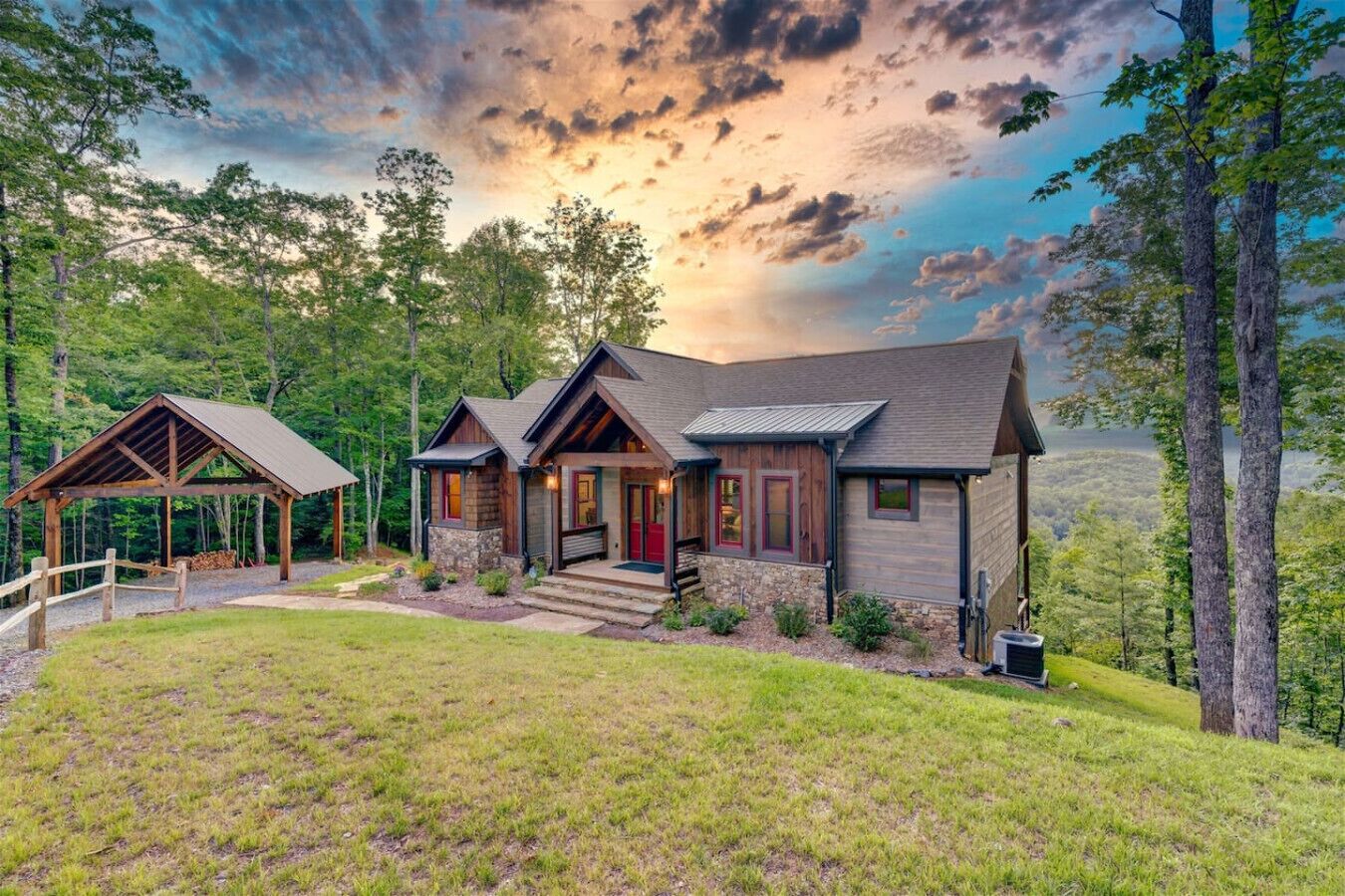 A two-story cabin with a stone foundation, wooden exterior, and a red door. It is surrounded by a well-maintained lawn and trees, with a covered porch area.