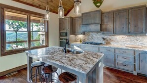 A kitchen with a large island, wooden cabinets, and a view of the outdoors. - Luxury 3BR Mountain Cabin • Hot Tub • Game Room • Outdoor Fireplace (Epworth)