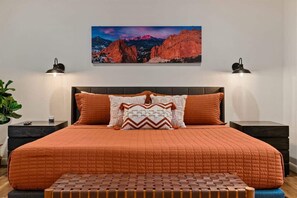 A bedroom with a large bed, two bedside tables, a nightstand, a wall-mounted lamp, and a painting of a mountain landscape. - Beautifully Decorated, Private Hot Tub! Pony Soldi (Sedona)