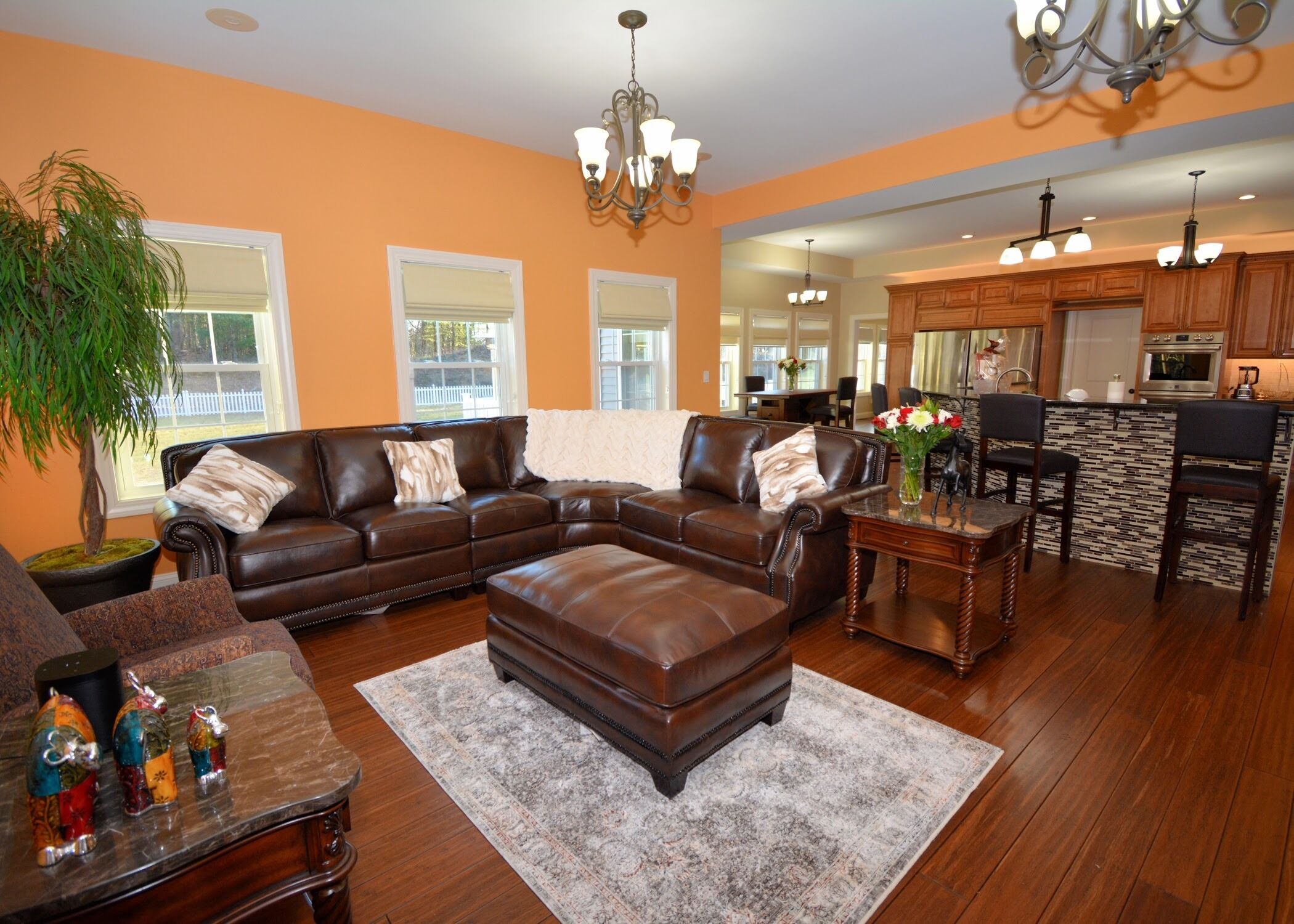 A spacious living room with a leather sectional sofa, a coffee table, and a rug. There is a dining area with a table and chairs, and a kitchen with wooden cabinets and a countertop.