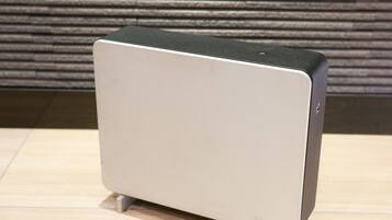 A modern, minimalist air purifier with a sleek design, placed on a wooden floor against a textured wall.
