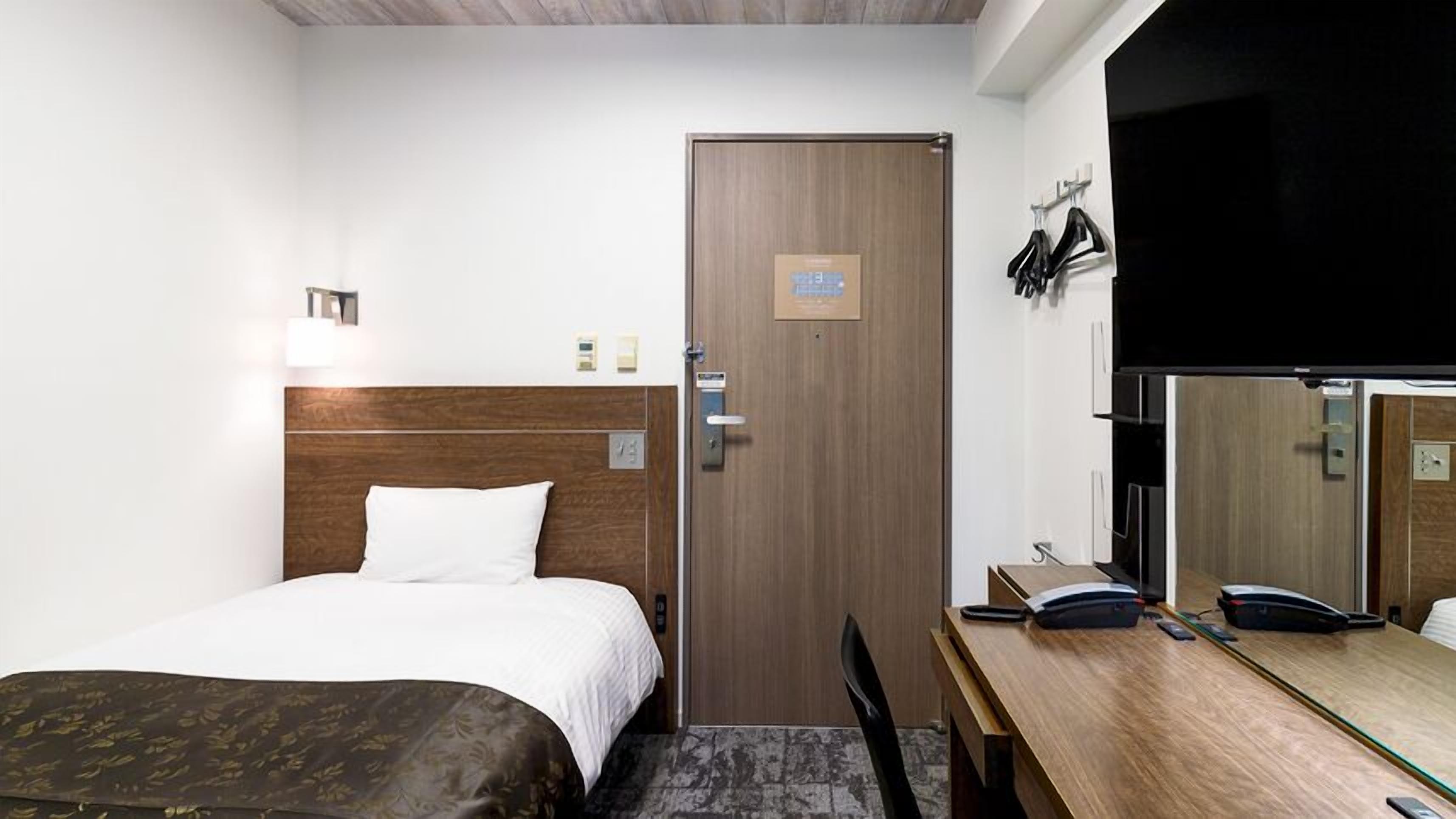 Habitació d'hotel amb llit, escriptori, cadira, porta i mirall.