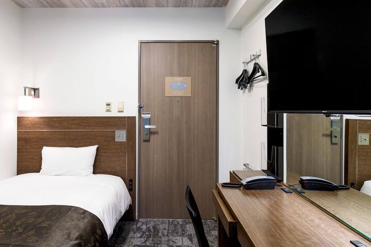 A hotel room with a bed, a desk, a chair, a door, and a mirror.