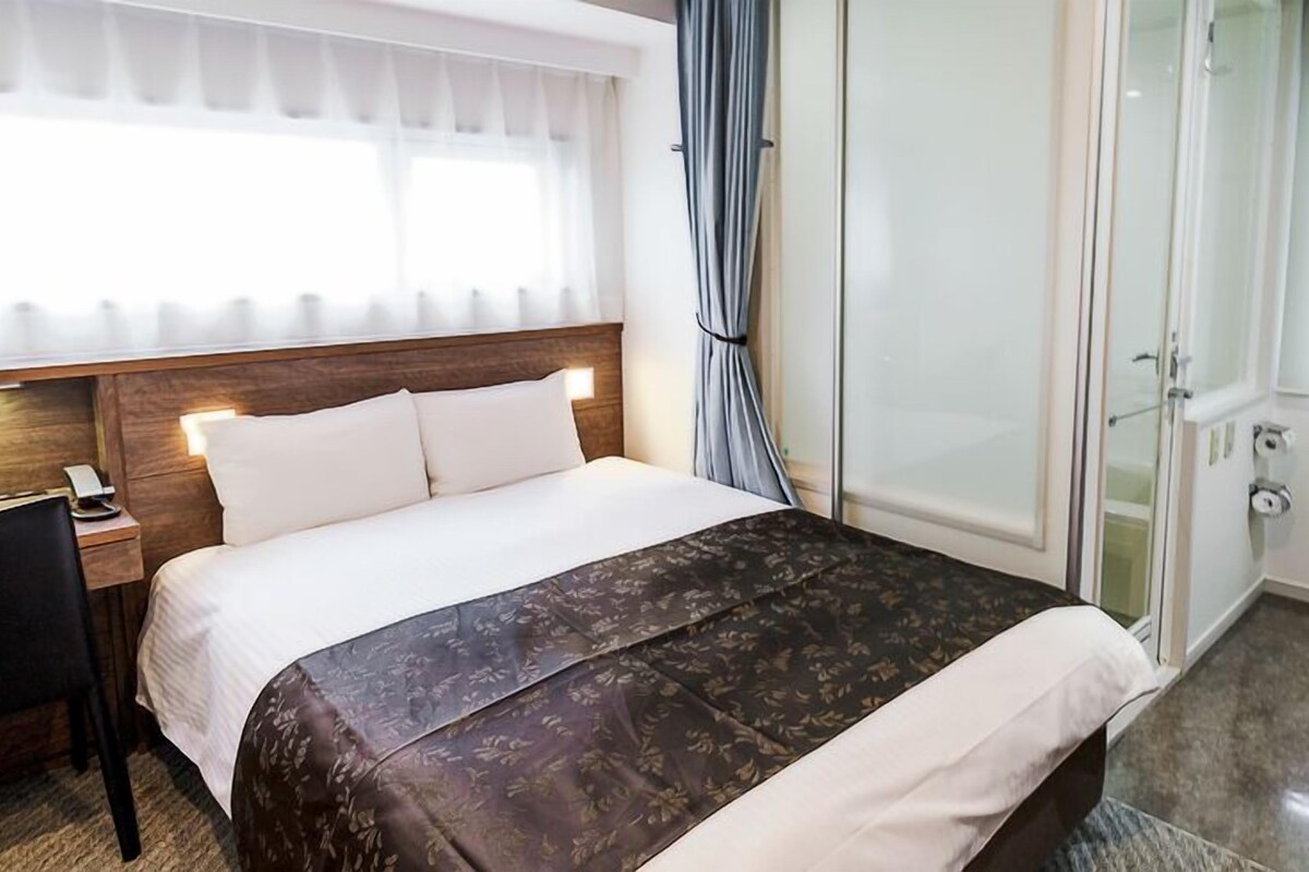 A hotel room with a bed, bedside table, and a shower area.