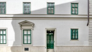A two-story building with a white facade, green window frames, and a central entrance with a green door. - Spacious 2BR + Office near Stephansplatz & Kohlmarkt, by Blueground (Vienna)
