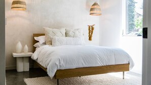 A bedroom with a wooden bed, white bedding, two hanging lamps, a bedside table with vases, and a view of the outdoors. - Silo at Hara Homes Luxury Stay (Leavenworth)