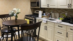 Una cocina con armarios blancos, microondas, estufa y un comedor con mesa y sillas.