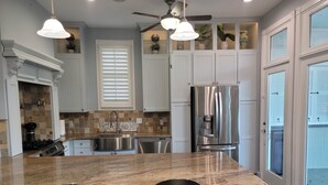 A modern kitchen with white cabinets, a stainless steel refrigerator, and a granite countertop. - Historic Hideaway with pool!  Close to beaches and downtown. (Galveston)