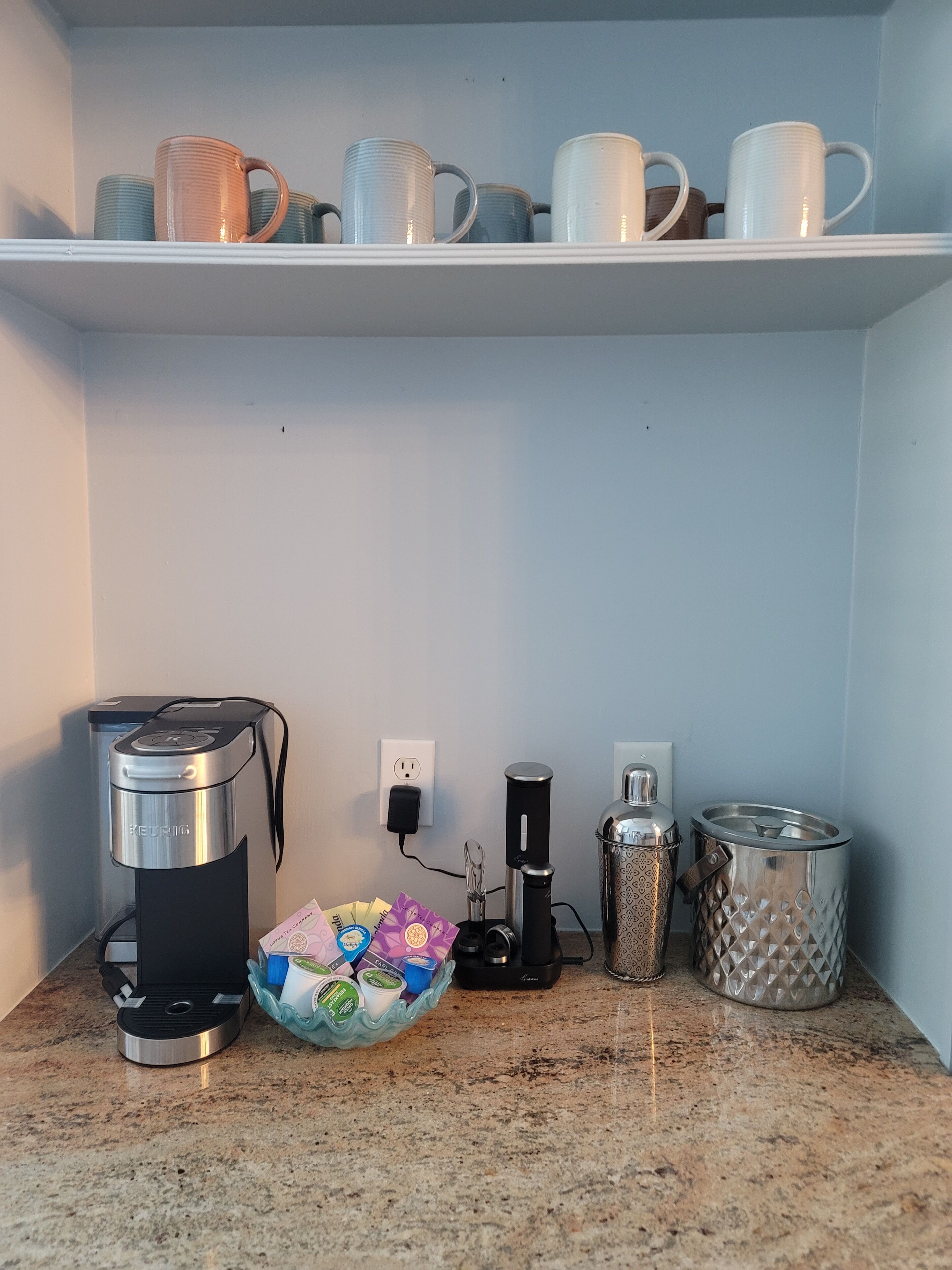 Una cocina con cafetera, hervidor y soporte para cápsulas de café en la encimera.
