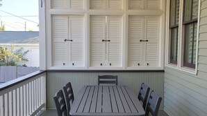 A covered patio with a table and chairs, a ceiling fan, and white shutters on the walls. - Historic Hideaway with pool!  Close to beaches and downtown. (Galveston)