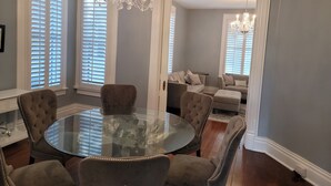 A dining room with a round glass table, six upholstered chairs, a chandelier, and a view into a living area with a sofa and a chandelier. - Historic Hideaway with pool!  Close to beaches and downtown. (Galveston)