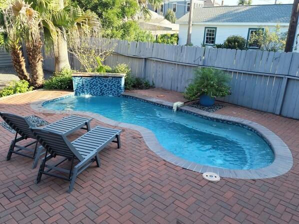 A backyard with a swimming pool, two lounge chairs, and a decorative tile border.