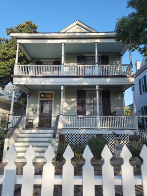 A two-story house with a front porch, a covered entryway, and a small front yard with a white picket fence.