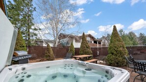 Un patio trasero con un jacuzzi, una parrilla para barbacoa y una mesa de madera.