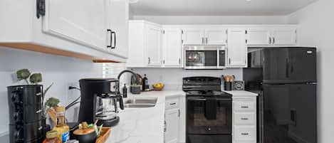 A modern kitchen with white cabinets, a black refrigerator, a stove, and a microwave.