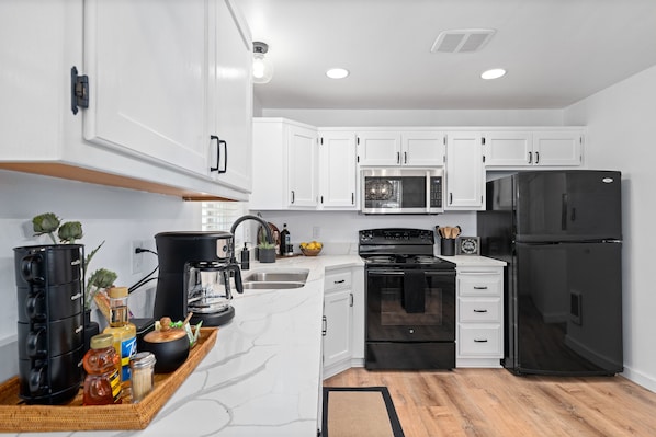 A modern kitchen with white cabinets, a black refrigerator, a stove, and a microwave.