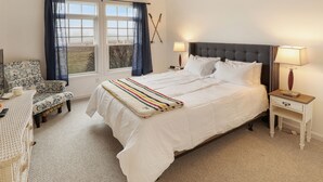 A bedroom with a large bed, two bedside tables, a chair, and a window with curtains. - Condo close to hiking, river, with mountain views (Thornton)