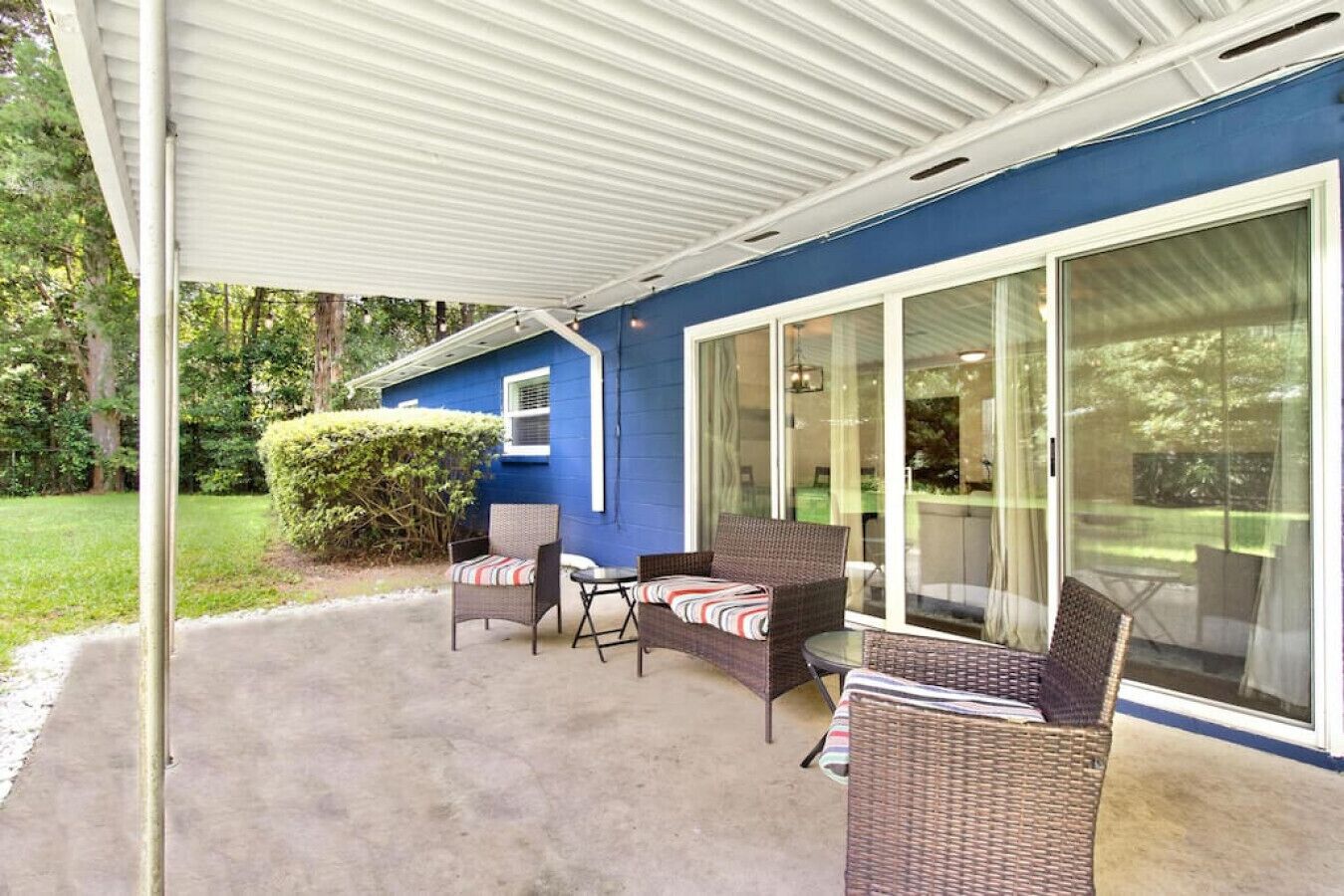 A covered patio with wicker furniture, a sliding glass door, and a blue exterior wall.