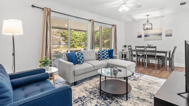 Uma sala de estar moderna com sofá seccional, mesa de centro, área de jantar com mesa e cadeiras, e janelas amplas com cortinas.