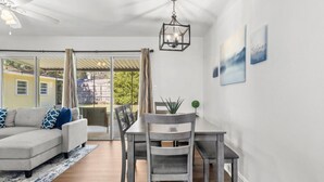 Uma sala de estar moderna com um sofá seccional cinza, uma mesa de jantar com cadeiras, um ventilador de teto e um lustre.