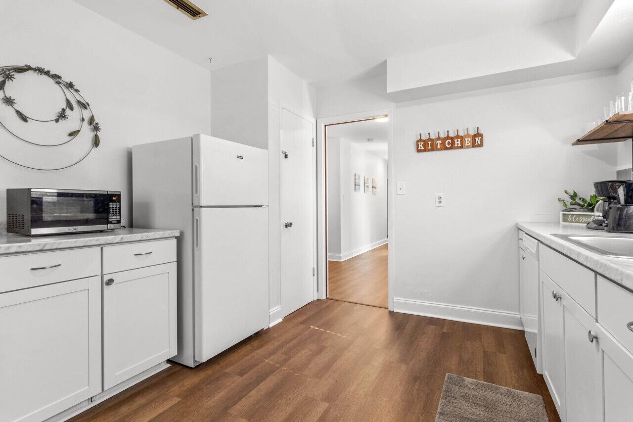 A modern kitchen with white cabinetry, a microwave, a refrigerator, and a 'KITCHEN' sign.