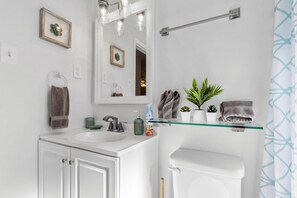 A bathroom with a white sink, mirror, towel rack, and a glass shelf with plants and toiletries.