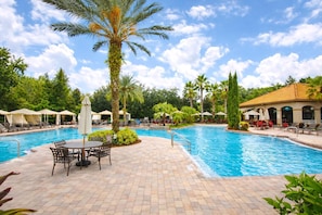 A swimming pool with lounge chairs and umbrellas, surrounded by palm trees and greenery. - 1361 Tuscana (Davenport)