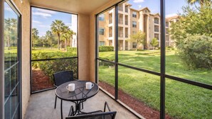 A balcony with a table and chairs, large windows, and a view of a well-maintained lawn and buildings. - 1361 Tuscana (Davenport)