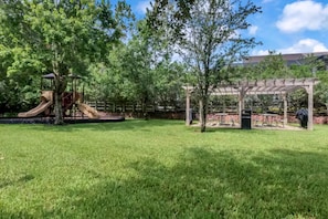 Un espacio al aire libre con césped, un parque infantil y una pérgola.