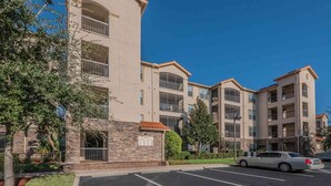 A multi-story residential building with balconies, a parking lot, and a clear blue sky. - 1361 Tuscana (Davenport)