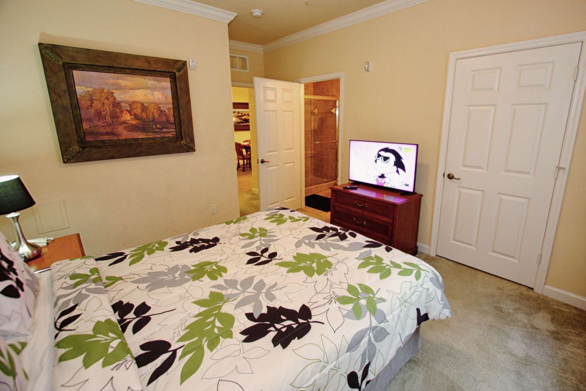 Un dormitorio con una cama, televisión, un cuadro y armario.