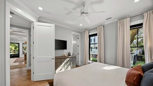 Une chambre à coucher avec un lit, une télévision, un ventilateur de plafond et une vue sur l’extérieur.