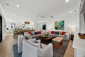 A spacious living room with a large sofa set, a dining area with wooden furniture, and a kitchen in the background. - 8 bedroom LUXURY IOP Home with Private POOL & Ocean VIEWS!! Steps from beach! (Isle Of Palms)