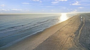 Une plage avec un large rivage sablonneux et des vagues douces, sous un ciel dégagé.