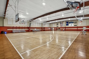 An indoor basketball court with a wooden floor, basketball hoops, and bleachers.