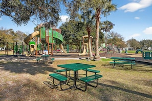 A playground with slides and swings, picnic tables, and trees.