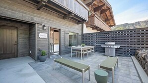 A modern outdoor patio with a dining table, benches, and a grill area.