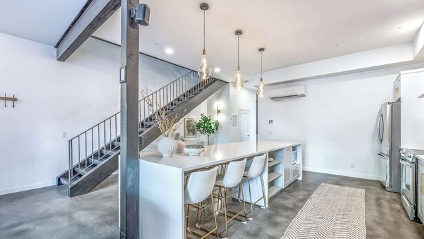 A modern kitchen with a central island, bar stools, and a staircase.