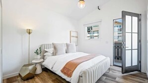 A modern bedroom with a bed, bedside tables, a floor lamp, and a view of the outside.