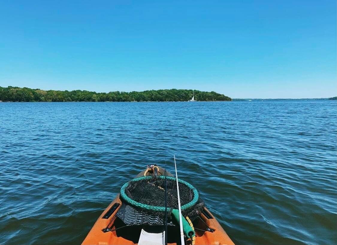 A boat on calm water with a green net and a white sail in the distance.