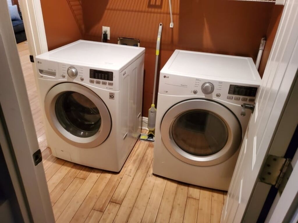 Dos lavadoras de carga frontal en un lavadero con suelo de madera y pared marrón.