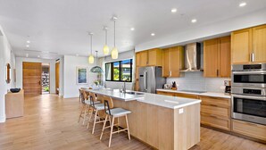 A modern kitchen with a large island, wooden cabinets, stainless steel appliances, and pendant lighting. - Maui Resort Rentals: 6 Total Bedrooms at Kaanapali’s Newest Luxury Residences, Steps from Beach & Resort Amenities! (Lahaina)